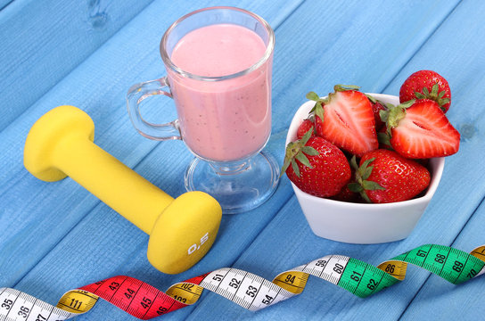 Fresh strawberries, milkshake, dumbbells and centimeter on blue boards, concept of healthy and sporty lifestyle