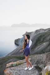 Naklejka premium Woman standing on a cliff with a stunning view of sea coast with background of the hills and mountains. She is happy and enjoying the moment of freedom