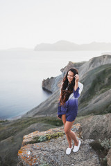 Naklejka premium Woman standing on a cliff with a stunning view of sea coast with background of the hills and mountains. She is happy and enjoying the moment of freedom