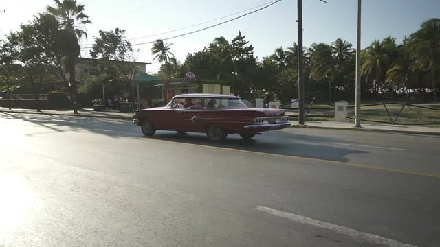 Red retro car convertible is riding on the central street of Varadero at sunset