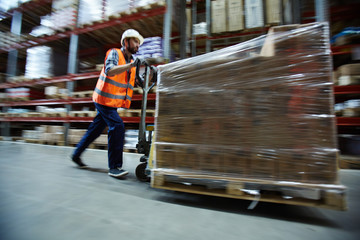 Loader in uniform pushing forklift with packed goods
