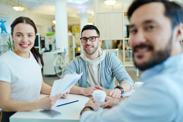 Portrait of three creative business people looking at camera and smiling during meeting in modern office
