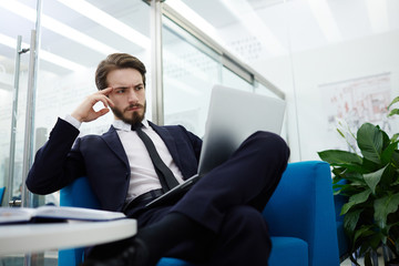 Pensive businessman with laptop reading online information in office