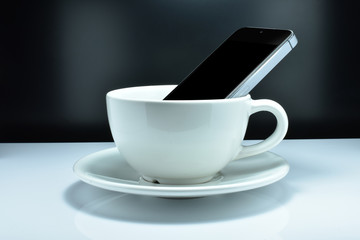 The smartphone is in the coffee mug. The Concept- Some people like to use a smartphone and drink coffee simultaneously.