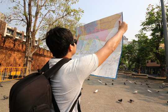 Back view of young asian tourist with backpack bag exploring a map in Tha Phae gate , Chiang Mai , Thailand