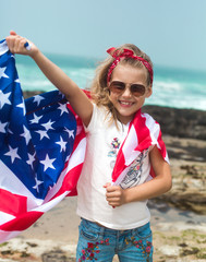Little smiling girl with long blond hair holds flying American flag on US Independence Day.