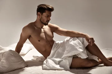 Fototapeten Schöner, muskulöser Mann, der auf dem weichen Bett posiert © konradbak