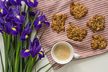 Homemade oatmeal cookies on a striped fabric background on a table with a mug of fragrant freshly brewed coffee with spices and flowers of purple iris.