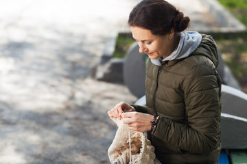 Young woman knits knitting on a walk in the city park on a summer day