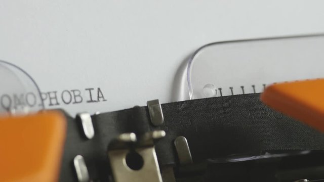 Close up footage of a person writing HOMOPHOBIA on an old typewriter, with sound...