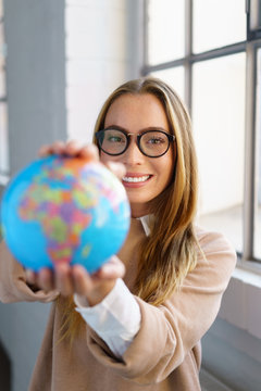 selbstbewusste frau mit brille hält einen globus in den händen