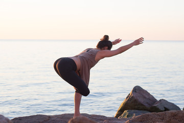 fitness mixed race asian woman in yoga pose on the morning beach, beautiful fit woman practice fitness exrxise stones, morning sea or ocean background