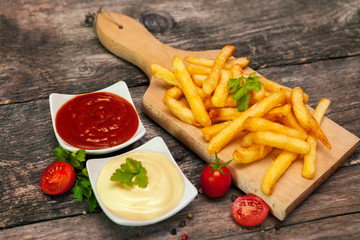 French fries on chopping board with tomato sauce and mayonnaise in bowls and cherry tomato
