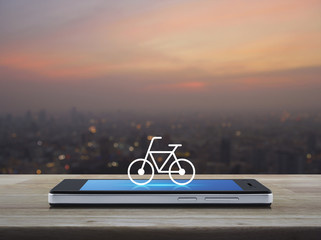Bicycle flat icon on modern smart phone screen on wooden table over blur of cityscape on warm light sundown, Bike shop online concept