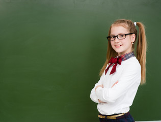 Happy girl standing near empty green chalkboard. Space for text