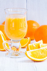 Orange juice in a glass on a white wooden table with whole and sliced oranges