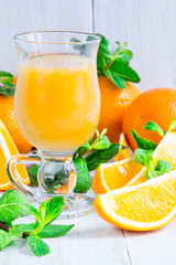 Orange juice in a glass on a white wooden table with whole and sliced oranges