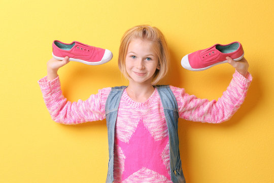 Funny teenager girl holding shoes on yellow background
