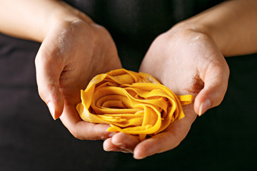 Fresh pasta in woman hands. Woman holding raw tagliatelle on a dark background.