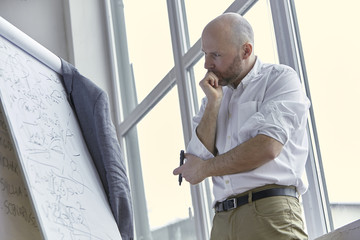 Fototapeta premium Thoughtful Bald Businessman Looking Carefully at the Board