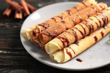 Tasty rolled pancakes with chocolate on plate
