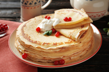 Tasty pancakes with cream and berries on table