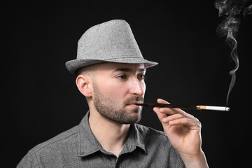 Handsome man smoking cigarette on dark background