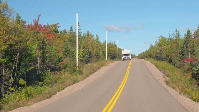 POV, CLOSE UP: RV car driving on empty highway running through lush dense mixed conifer and deciduous forest on sunny autumn day. Road passing through vast fall foliage woodland in Nova Scotia, Canada