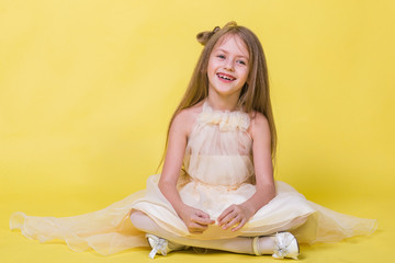 Obraz na płótnie Canvas Teenager girl in a dress on a yellow background posing for the camera and sits on the floor