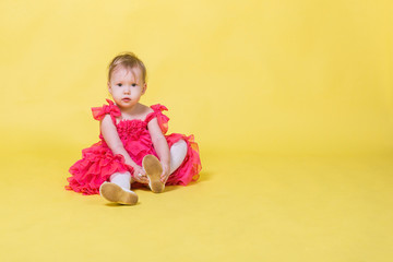 Girl toddler in a pink dress on a yellow background wearing the shoes on his feet