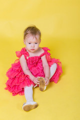 Girl toddler in a pink dress on a yellow background wearing the shoes on his feet
