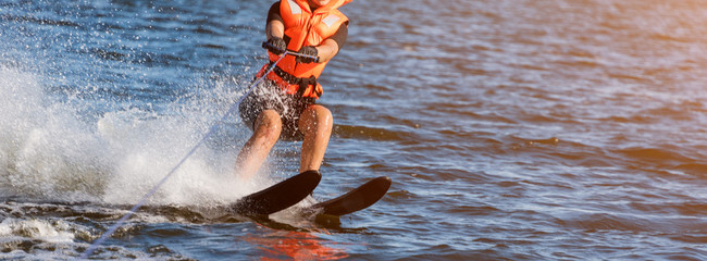 Woman riding water skis closeup. Body parts without a face. Athlete water skiing and having fun. Living a healthy lifestyle and staying active. Water sports theme. Summer by the sea. Banner for - Powered by Adobe