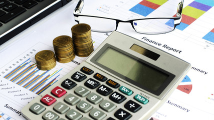 Close up of Coins stack and calculator and labtop with eyeglasses on financial chart backgrounds