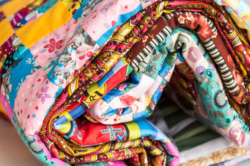 patchwork, sewing and fashion concept - macro of bright beautiful multi-colored quilt rolled up in the tube at shop, warehouse of finished stitched textile products, side view