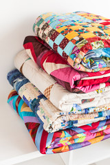 patchwork, quilting and fashion concept - close-up on beautiful colorful blankets folded and stored in several rows in height for storage, sale of stitched textile products on white background