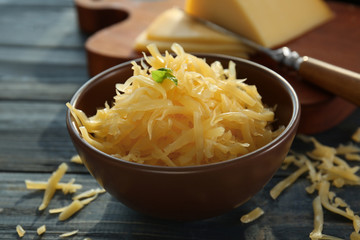 Bowl with grated cheese on wooden table