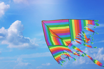 Rainbow kite flying in blue sky with clouds. Freedom and summer holiday concept