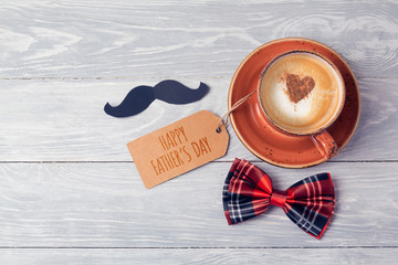 Fathers day background with coffee cup, note and bow on wooden table. View from above. Flat lay