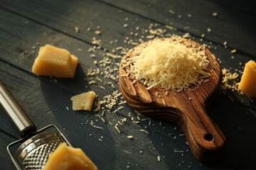 Wooden board with cheese and grater on table