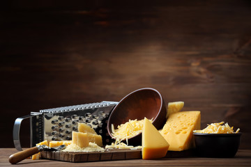 Composition of grater, cutting board and bowls with cheese on wooden background