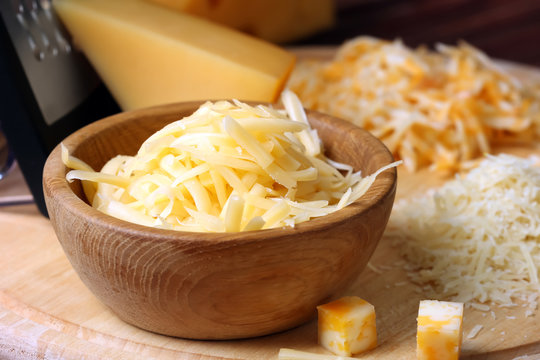 Wooden bowl with grated cheese on board