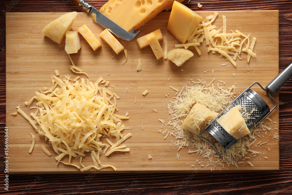 Wall mural Cutting board with cheese, grater and knife on wooden background