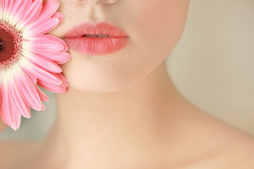 Beautiful young woman with flower on blurred background, closeup