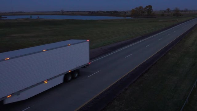 AERIAL, CLOSE UP: Personal car and a semi trucks driving on empty interstate highway in the dark. Lorry with freight container trailer transporting goods and shipping load across the country at night