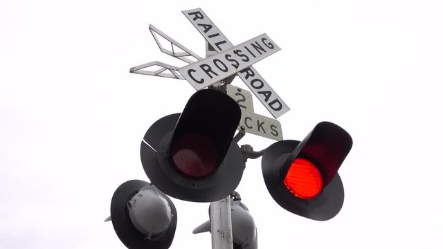 CLOSE UP Railroad crossing traffic sign with flashing red lights and barrier rising against the sky. Traffic sign on road and railway intersection. Traffic control on railway crossing in United States