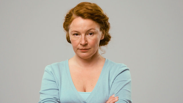 Mid aged actress showing emotions of doubt. Actress in studio shows the emotion of doubt. Close-up portrait of an actrees in light blue jumper. Actress with red curly hair shows the emotion of doubt.