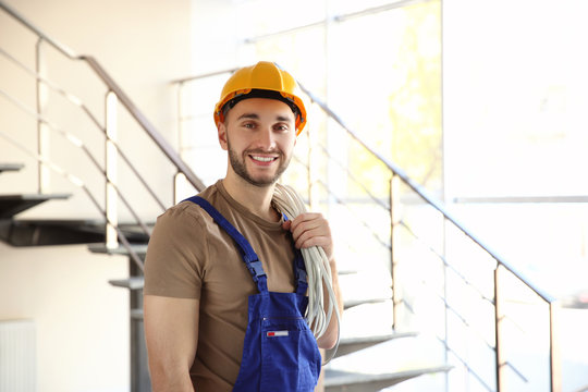 Young smiling electrician holding bunch of wires and standing in light room