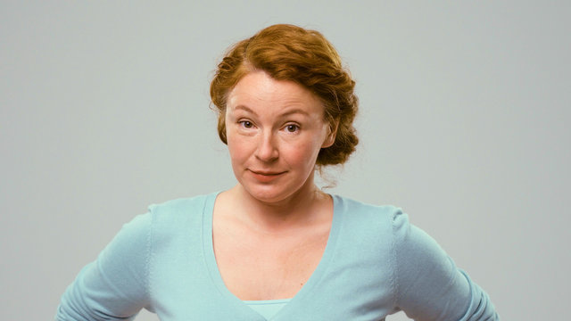 Mid aged actress showing emotions of claim. Actress in studio shows the emotion of claim. Close-up portrait of an actrees in light blue jumper. Actress with curly red hair shows the emotion of doubt.