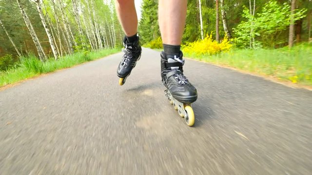 Start inline skating on smooth asphalt in the forest. Close up view to light skin man legs quick movement of inline boots.