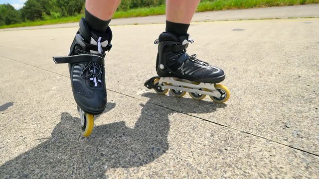 Mans legs roller skating on the asphal. Close up view to quick movement of inline boots.